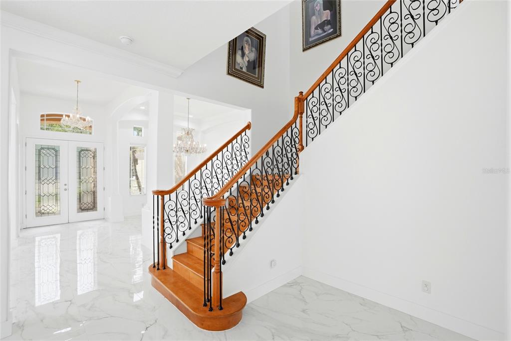A grand foyer features white marble floors, a wooden staircase with iron railings, and chandeliers — 11637 BRISTOL CHASE DRIVE, TAMPA, FL