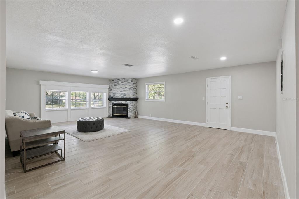 A spacious living room features light wood-look tile flooring, a corner stone fireplace, and windows — 1033 CRYSTAL BOWL CIRCLE, CASSELBERRY, FL