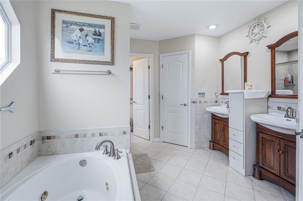 A bathroom features a jetted tub, two wood vanities with sinks, and tiled flooring — 2028 CANYON RIM PLACE, MIDDLEBURG, FL