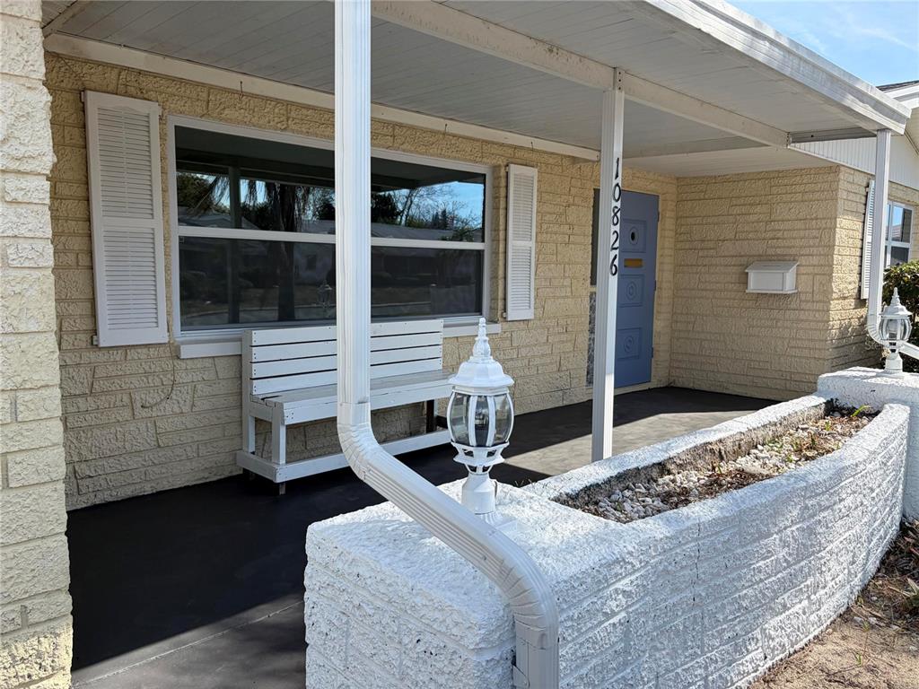A covered front porch features a white bench, a brick planter, and a blue door — 10826 PICCADILLY ROAD, PORT RICHEY, FL