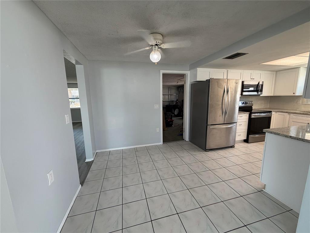 A kitchen and dining area with light gray walls, white cabinets, and tiled flooring — 10826 PICCADILLY ROAD, PORT RICHEY, FL