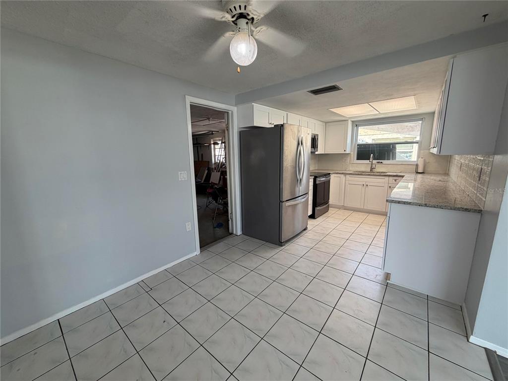 A kitchen with white cabinets, granite countertops, stainless steel appliances, and light-colored tile flooring — 10826 PICCADILLY ROAD, PORT RICHEY, FL