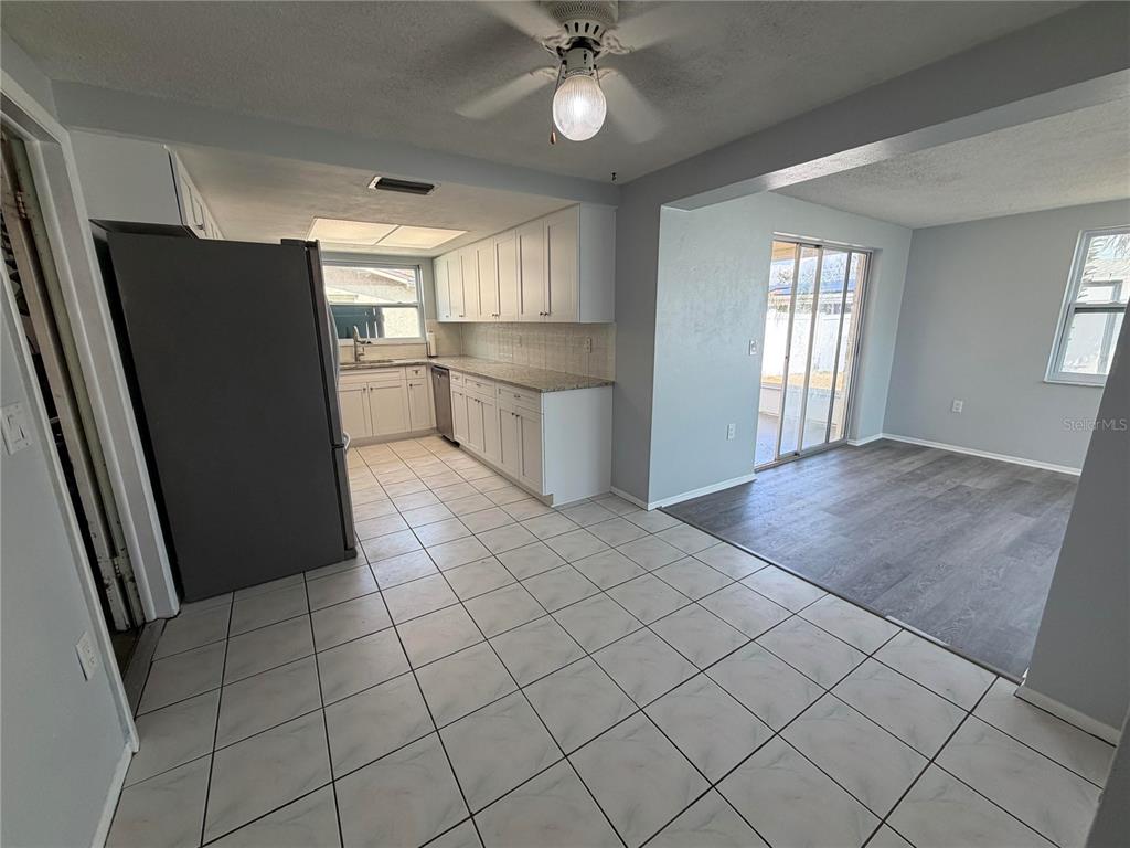 A kitchen with white cabinets and tile flooring transitions into a dining area with wood-look flooring — 10826 PICCADILLY ROAD, PORT RICHEY, FL