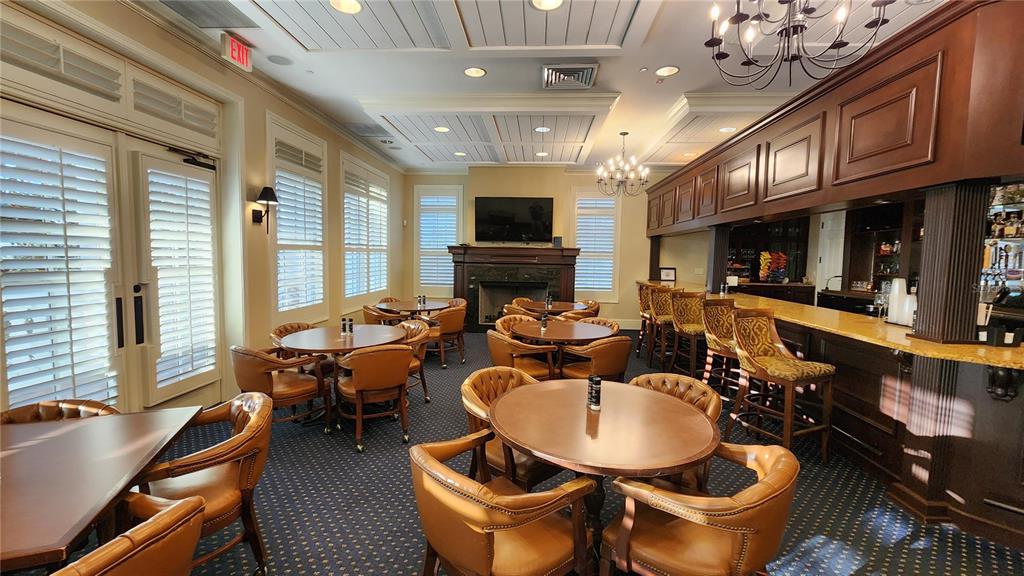 A restaurant interior features round tables, leather chairs, a long bar, and a stone fireplace — ESTABLISHED BLINDS & DESIGN, SPRING HILL, FL