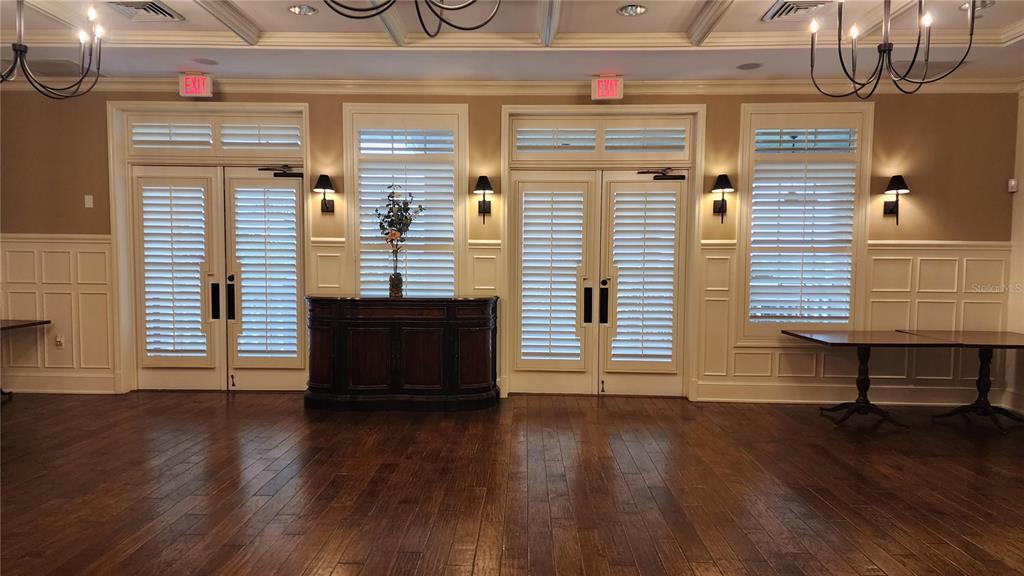 A room with hardwood floors, white wainscoting, shuttered doors, and two chandeliers — ESTABLISHED BLINDS & DESIGN, SPRING HILL, FL