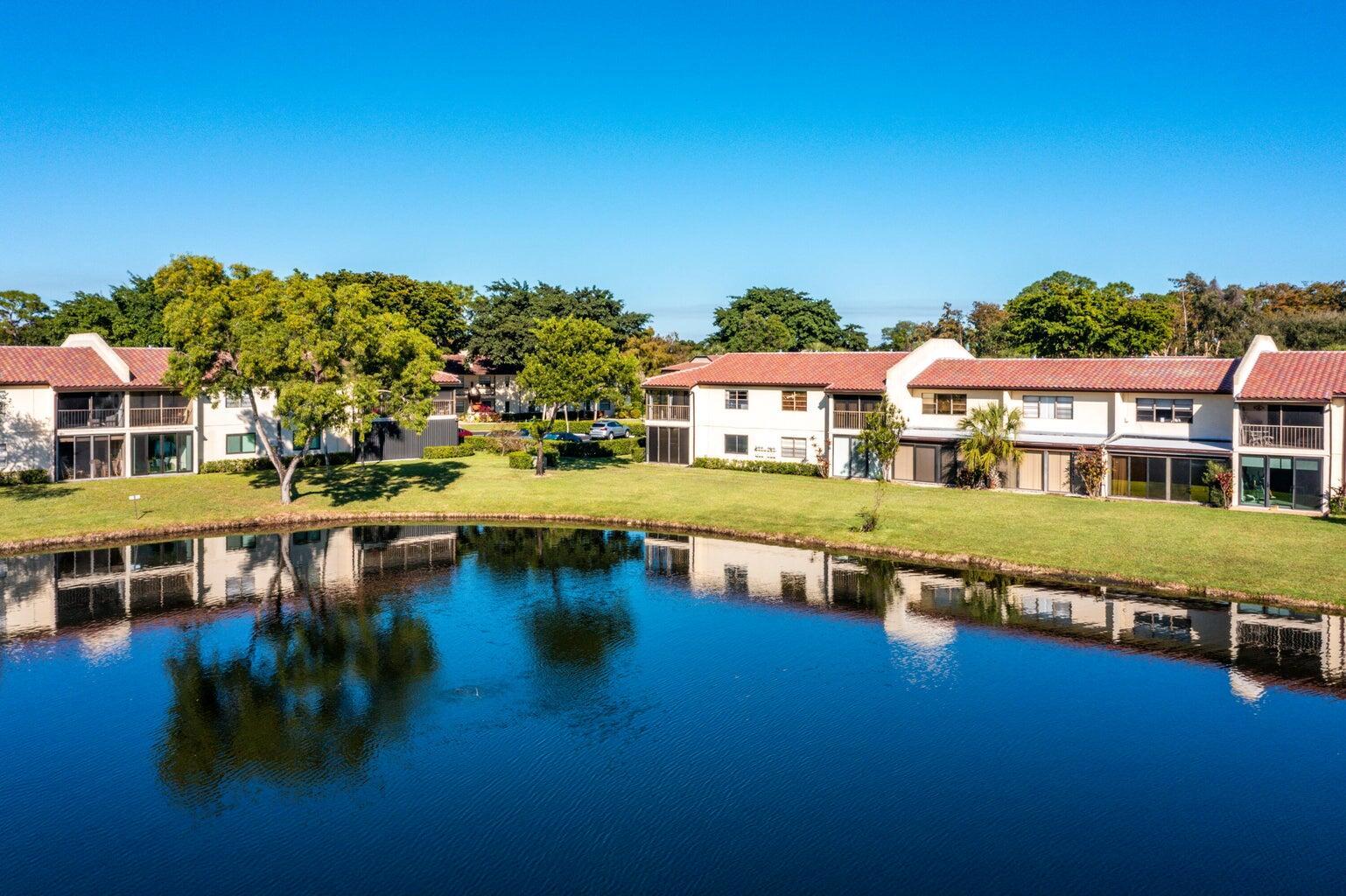 An aerial view of two-story apartment buildings overlooking a calm pond with green lawns — 21863 Arriba Real # k, Boca Raton FL 33433, BOCA RATON, FL