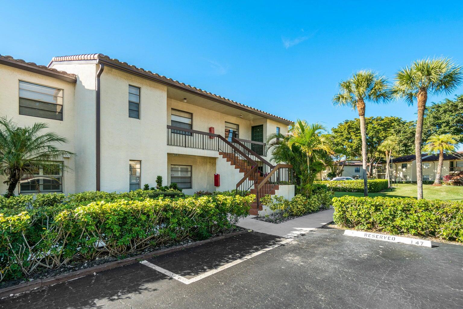 A two-story apartment building with exterior stairs, palm trees, and a reserved parking space — 21863 Arriba Real # k, Boca Raton FL 33433, BOCA RATON, FL
