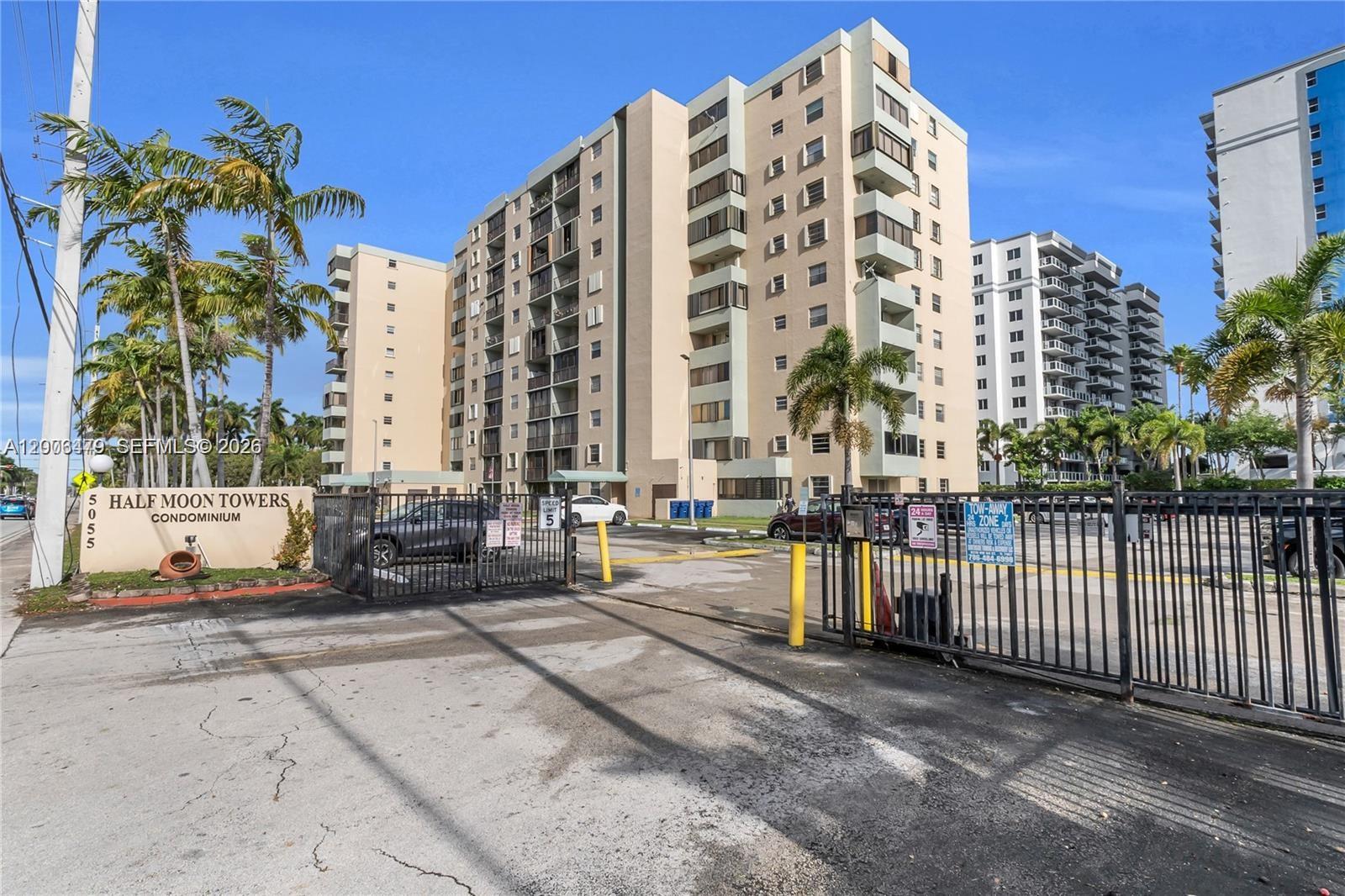A gated entrance leads to the Half Moon Towers condominium building with surrounding palm trees — 5055 NW 7th St # 504, Miami FL 33126, MIAMI, FL