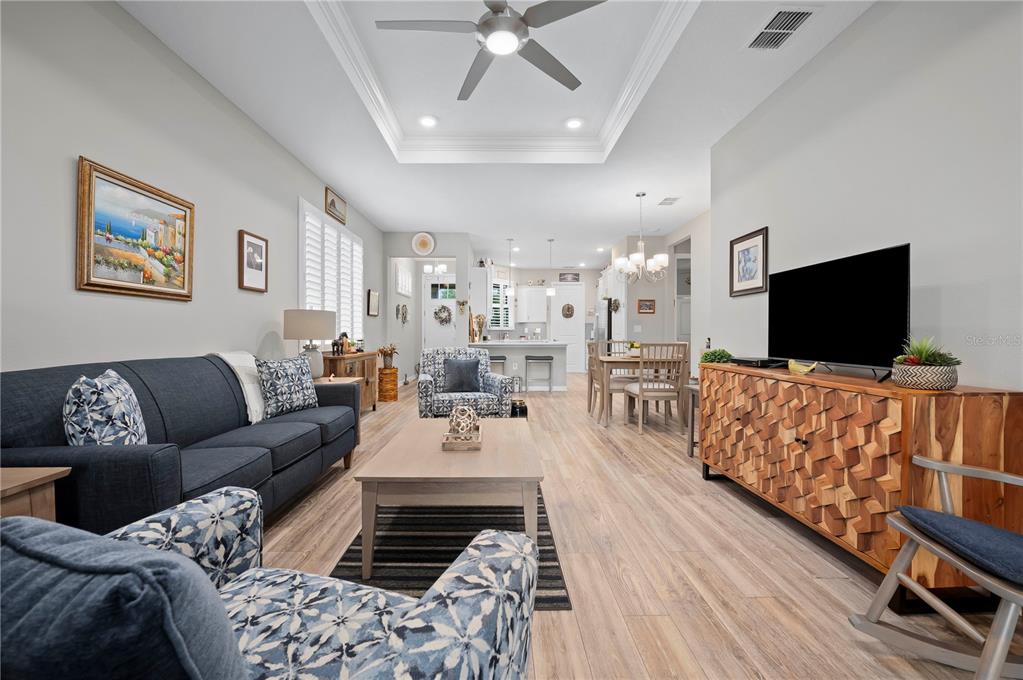 An open-concept living room features a dark blue sofa, patterned armchairs, and wood-look flooring — 7732 SW 86TH COURT, OCALA, FL