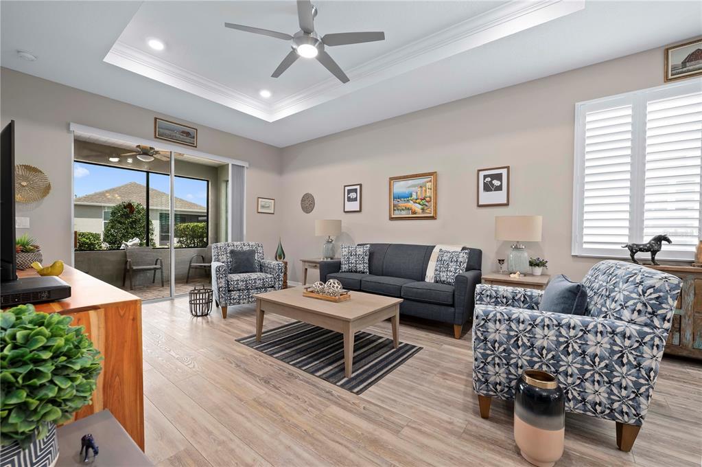 A living room features a tray ceiling, wood-look flooring, a dark sofa, and patterned armchairs — 7732 SW 86TH COURT, OCALA, FL