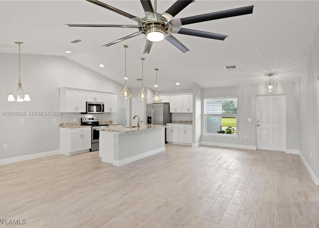 A kitchen with white cabinets, an island, and light wood-look flooring in an open room — 604 WILMINGTON, Cape Coral FL 33993, CAPE CORAL, FL