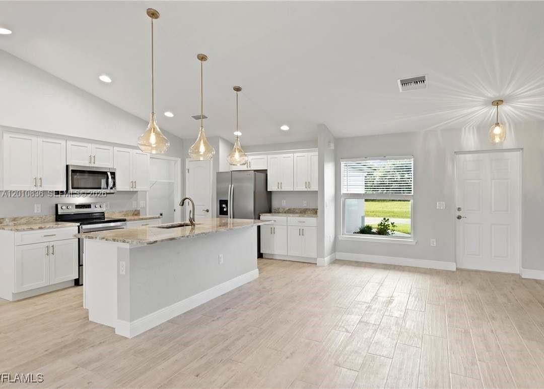 A kitchen features white cabinets, granite countertops, a center island, and light wood-look tile flooring — 604 WILMINGTON, Cape Coral FL 33993, CAPE CORAL, FL