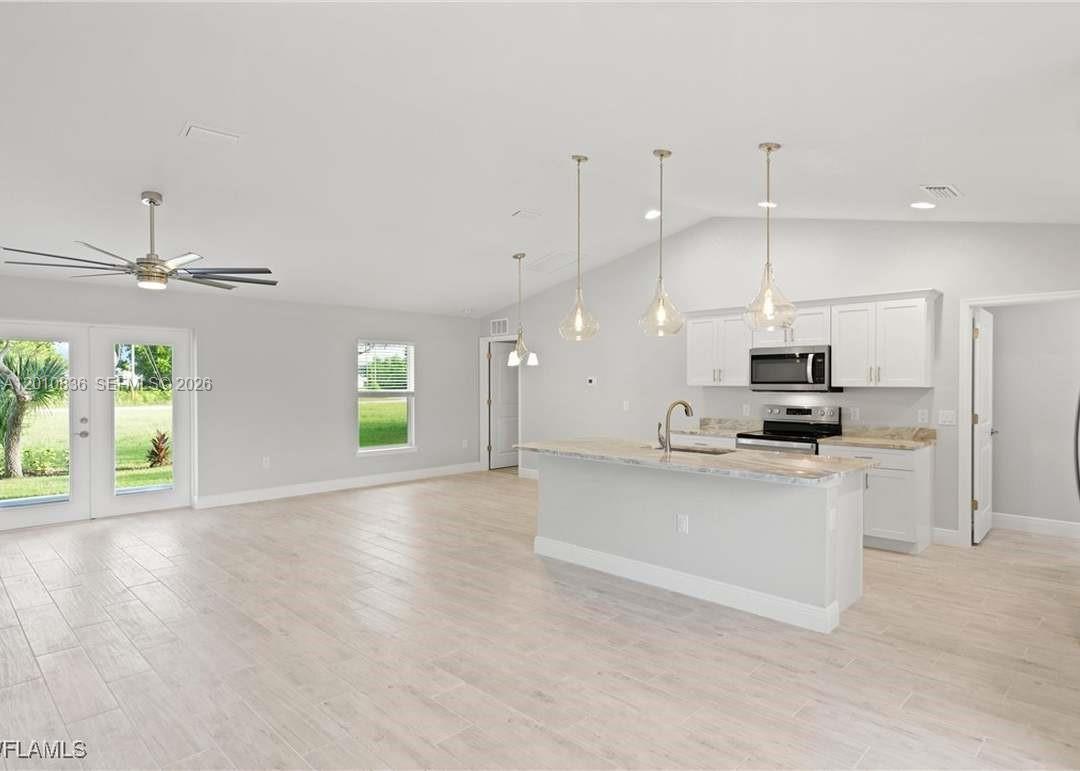 An open-concept kitchen features white cabinetry, a stone island, and light wood-look flooring — 604 WILMINGTON, Cape Coral FL 33993, CAPE CORAL, FL