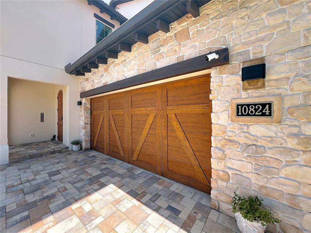A stone-faced house exterior features a wooden garage door and a paved driveway — 10824 ROYAL CYPRESS WAY, ORLANDO, FL