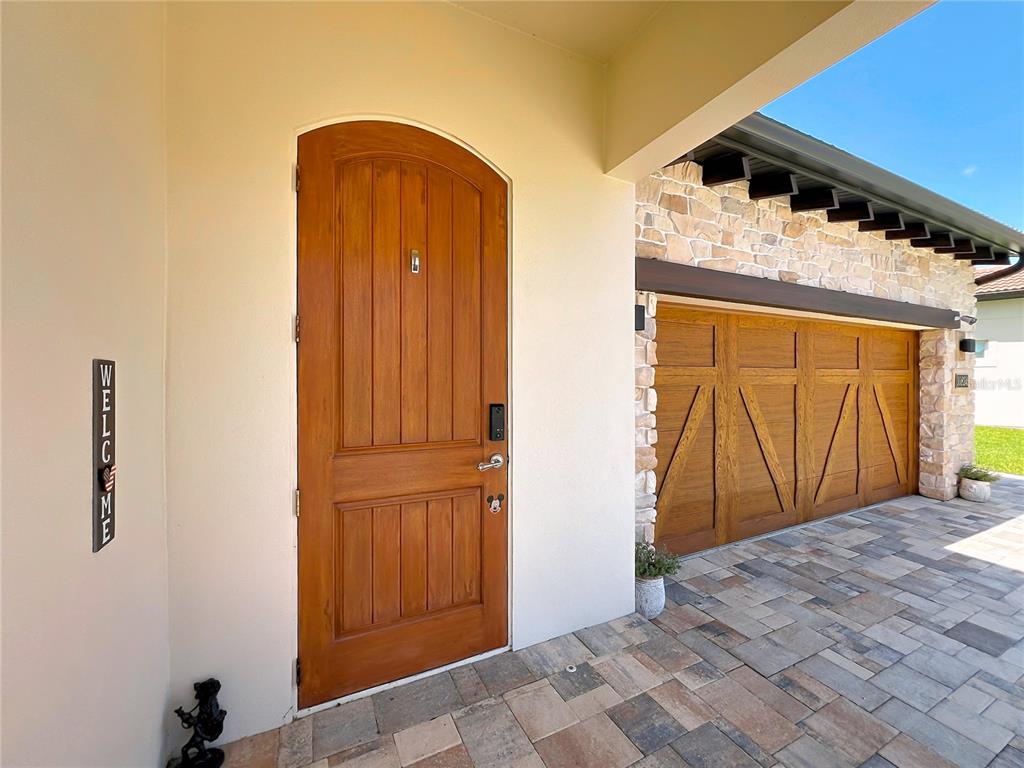 A wooden arched front door sits beside a stone-accented garage on a paved entryway — 10824 ROYAL CYPRESS WAY, ORLANDO, FL