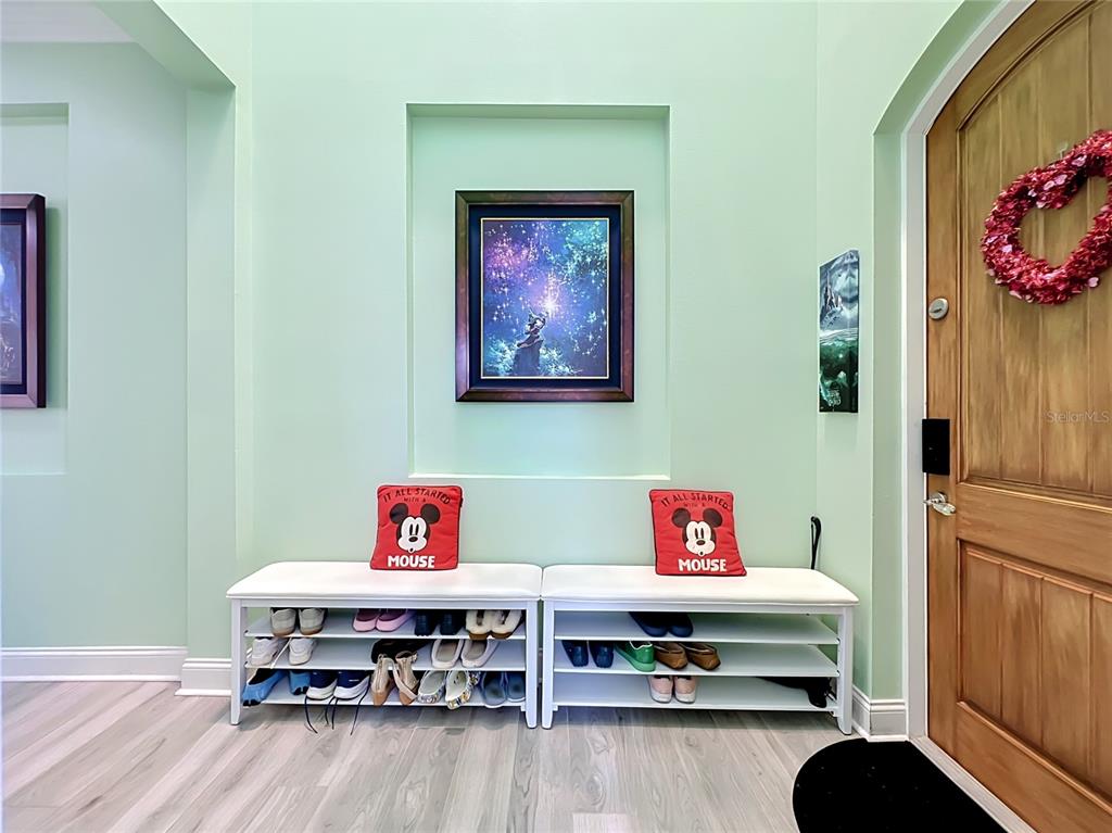 An entryway features light green walls, two white shoe benches, and Disney-themed wall art — 10824 ROYAL CYPRESS WAY, ORLANDO, FL