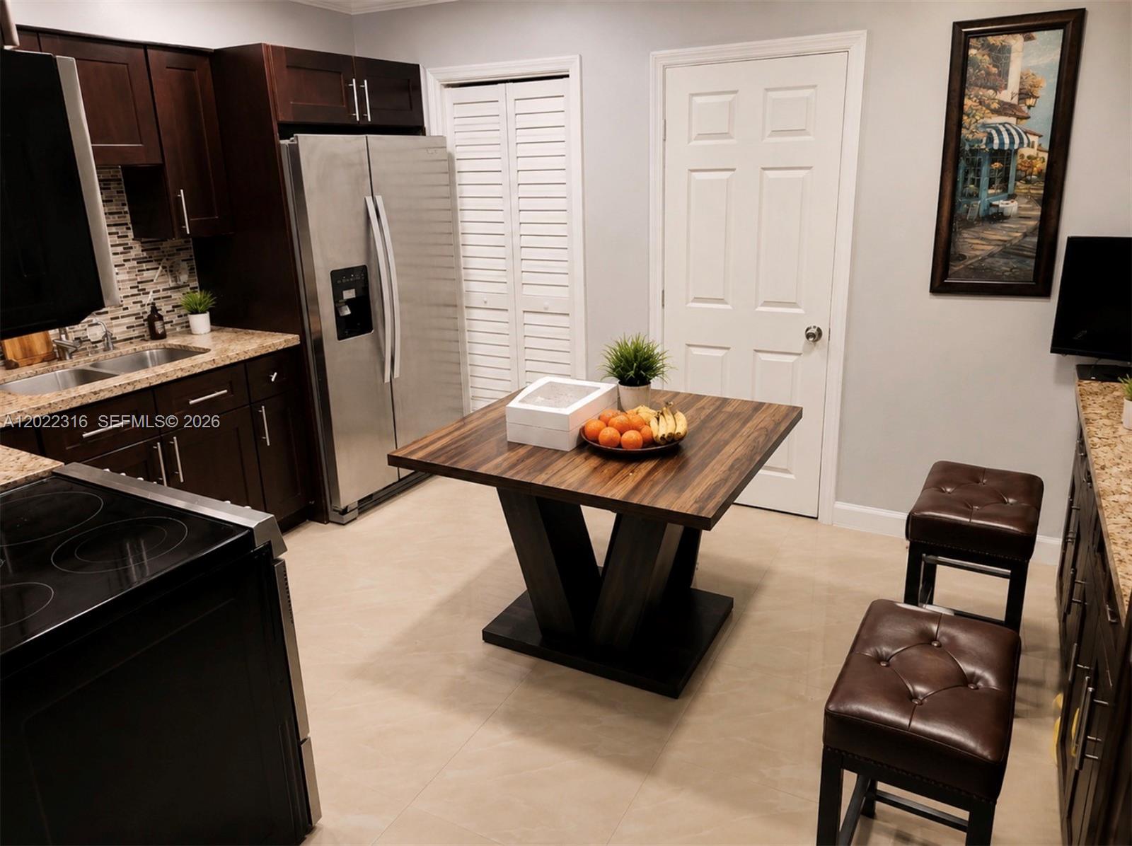 A kitchen features dark wood cabinets, stainless steel appliances, a square dining table, and stools — LAUDERHILL, FL