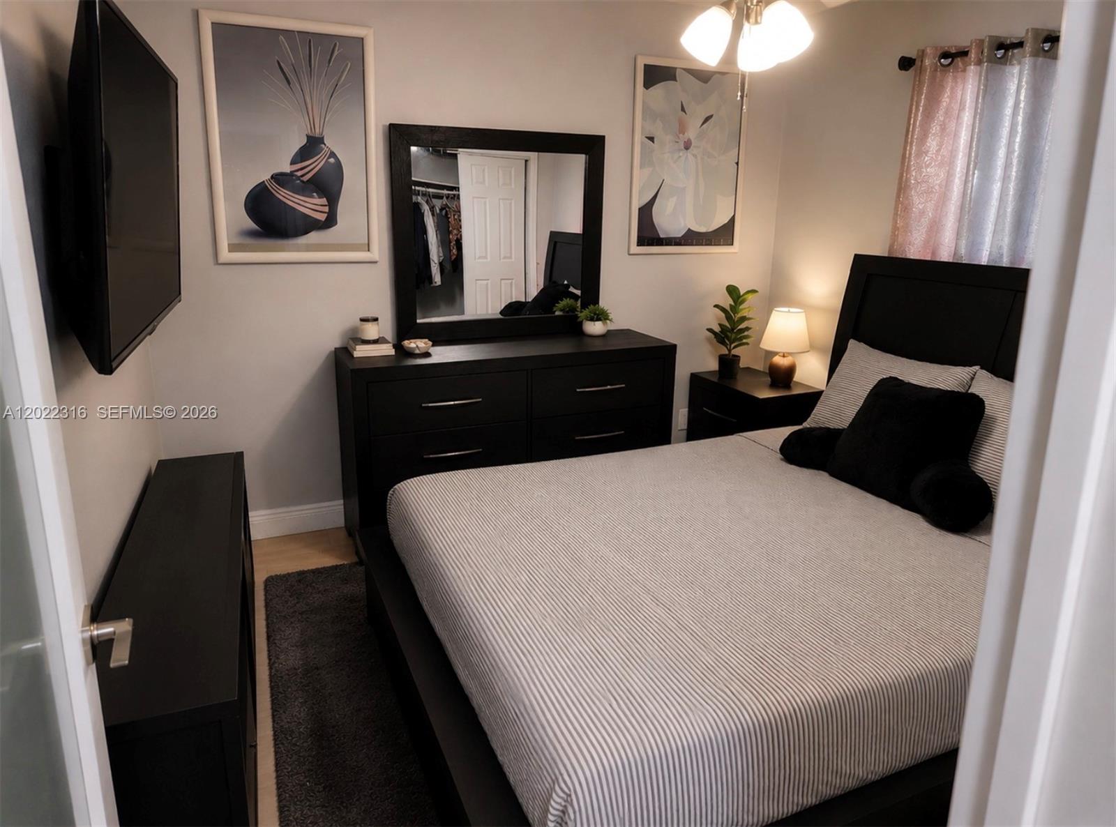 A bedroom features a black bed frame, matching dresser with mirror, and a wall-mounted television — LAUDERHILL, FL