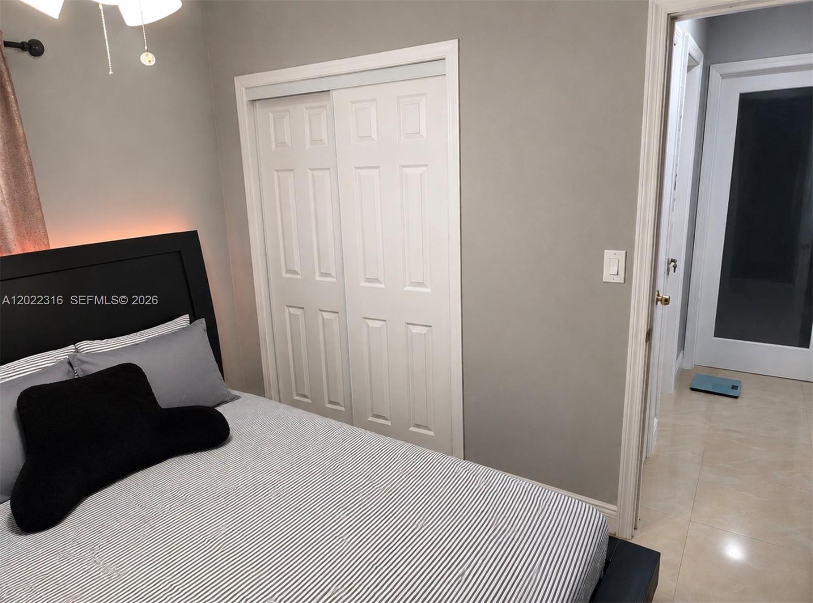 A bedroom features a striped bed, a black headboard, a white closet, and tile flooring — LAUDERHILL, FL