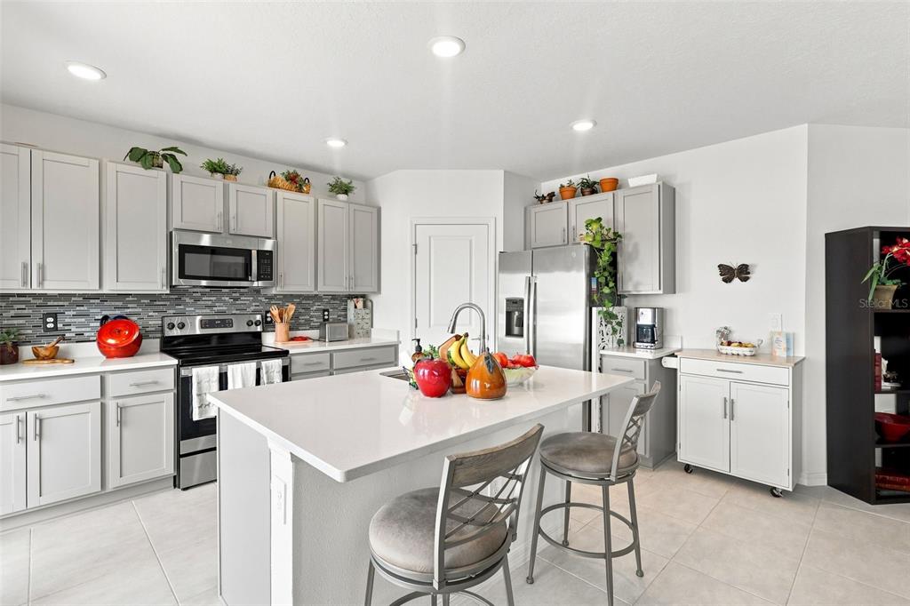 A kitchen features light gray cabinets, stainless steel appliances, a white island, and tile flooring — 124 CITRINE LOOP, KISSIMMEE, FL