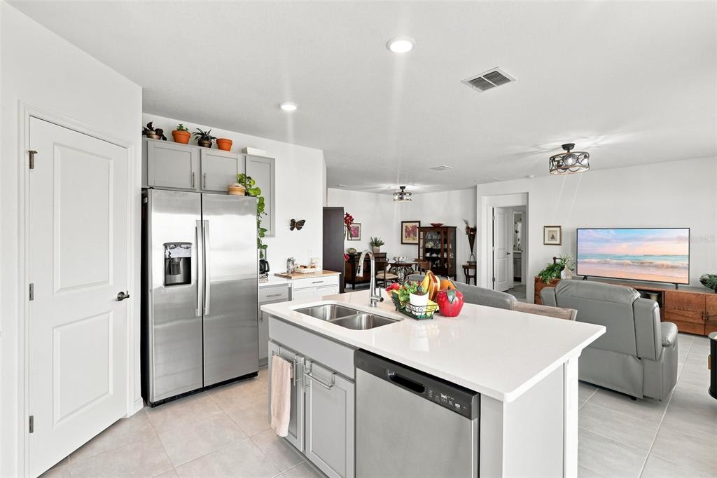 A kitchen with a central island, stainless steel appliances, and gray cabinetry opens to a living area — 124 CITRINE LOOP, KISSIMMEE, FL