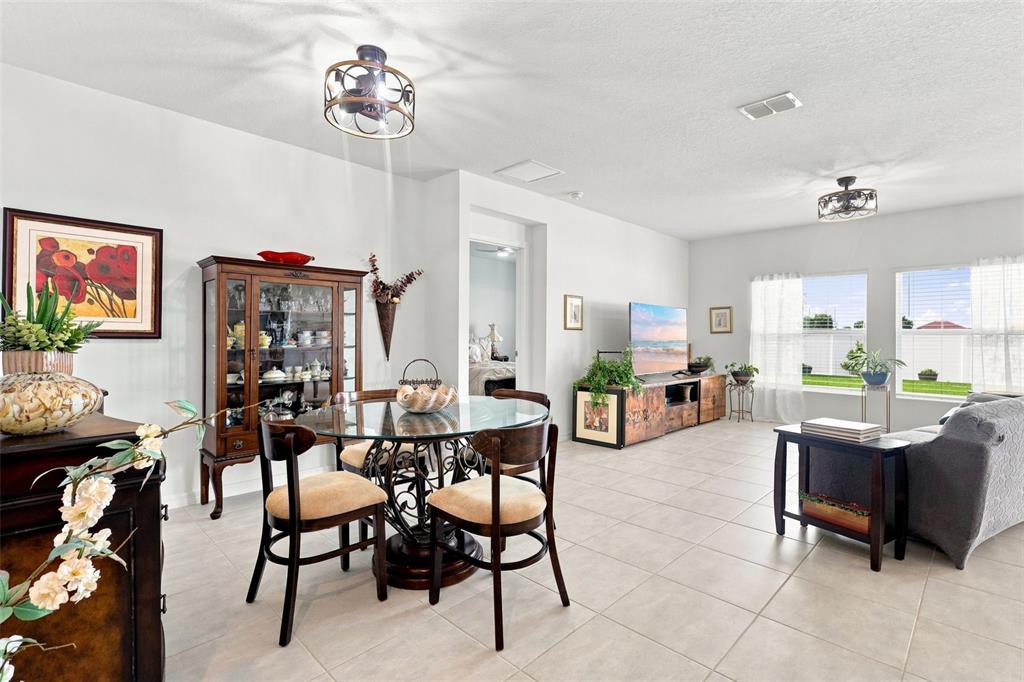 An open-concept living and dining area features tile flooring, a glass-topped table, and neutral walls — 124 CITRINE LOOP, KISSIMMEE, FL
