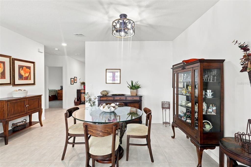 A dining room features a glass-topped table, wooden chairs, a china cabinet, and tile flooring — 124 CITRINE LOOP, KISSIMMEE, FL