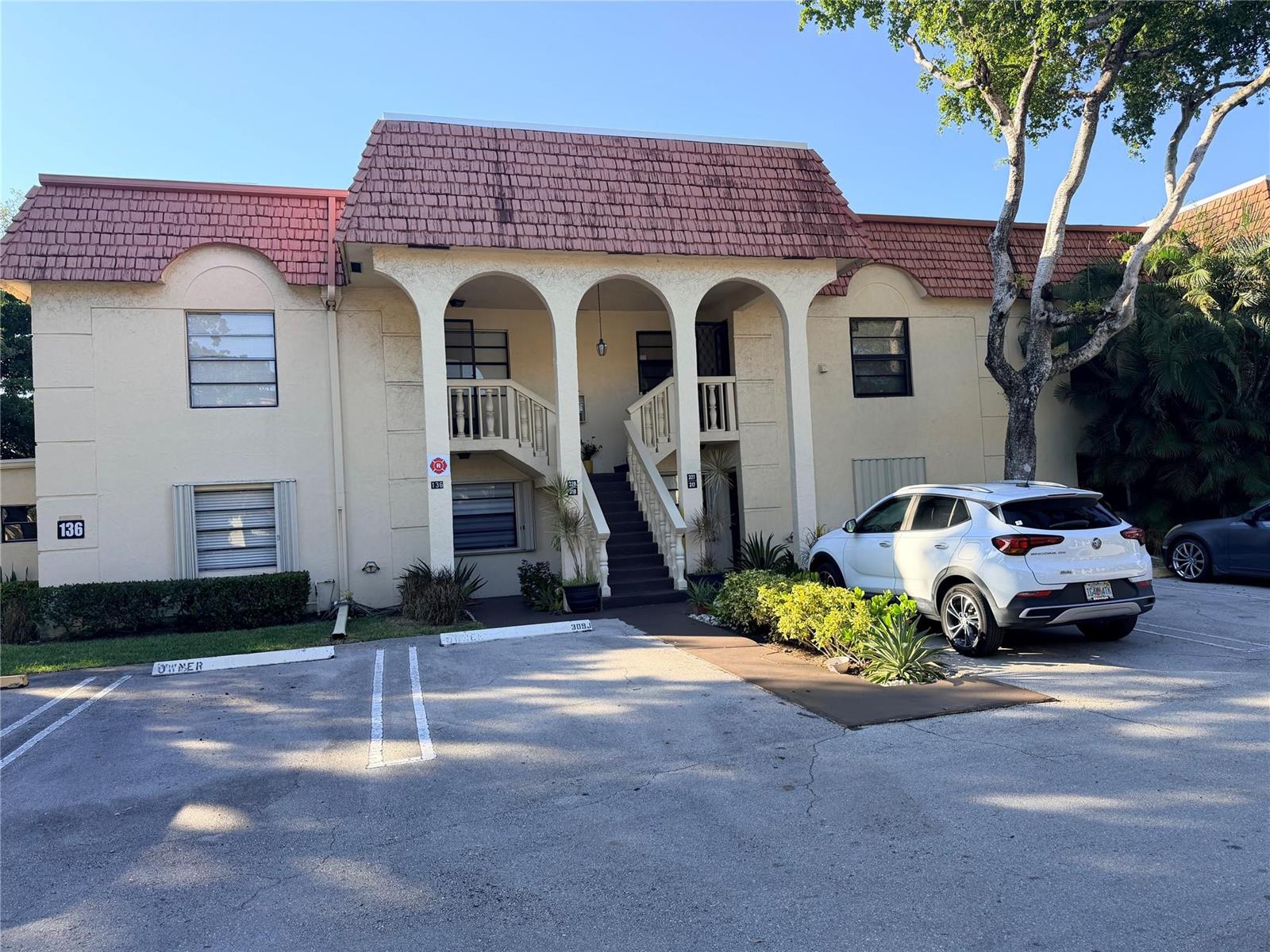 A two-story apartment building features a red mansard roof, arched entryway, and exterior stairs — 136 S Cypress Road # 317, Pompano Beach FL 33060, POMPANO BEACH, FL