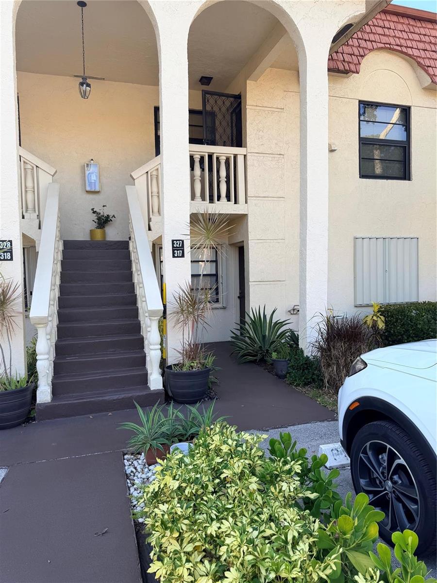 An exterior view of a two-story apartment building with a staircase and arched entryways — 136 S Cypress Road # 317, Pompano Beach FL 33060, POMPANO BEACH, FL