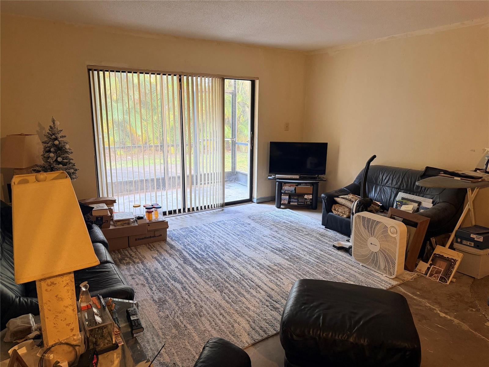 A living room features a large area rug, black leather furniture, and sliding glass doors — 136 S Cypress Road # 317, Pompano Beach FL 33060, POMPANO BEACH, FL