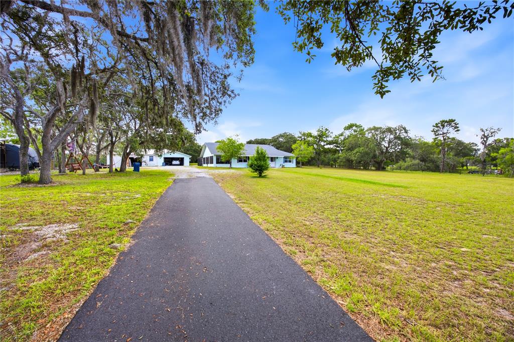 A paved driveway leads to a light blue house and a detached garage on a lawn — 6175 S CANNA LILY AVENUE, HOMOSASSA, FL