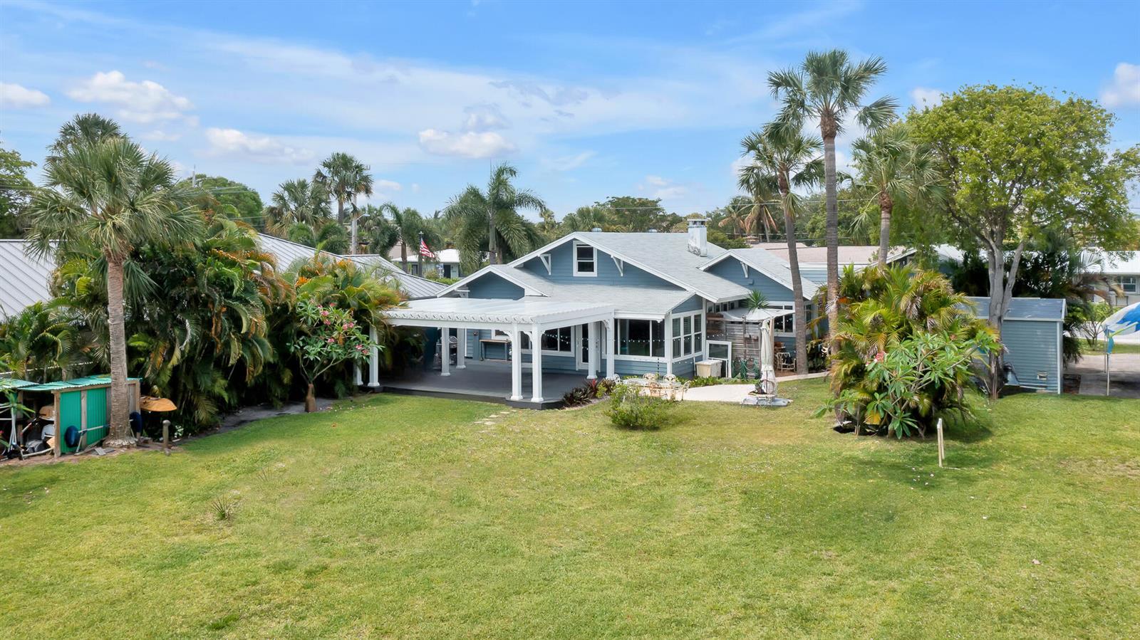 A blue house with a white pergola and a large grassy backyard under a blue sky — 1408 N Lakeside Drive, FL 33460, FL