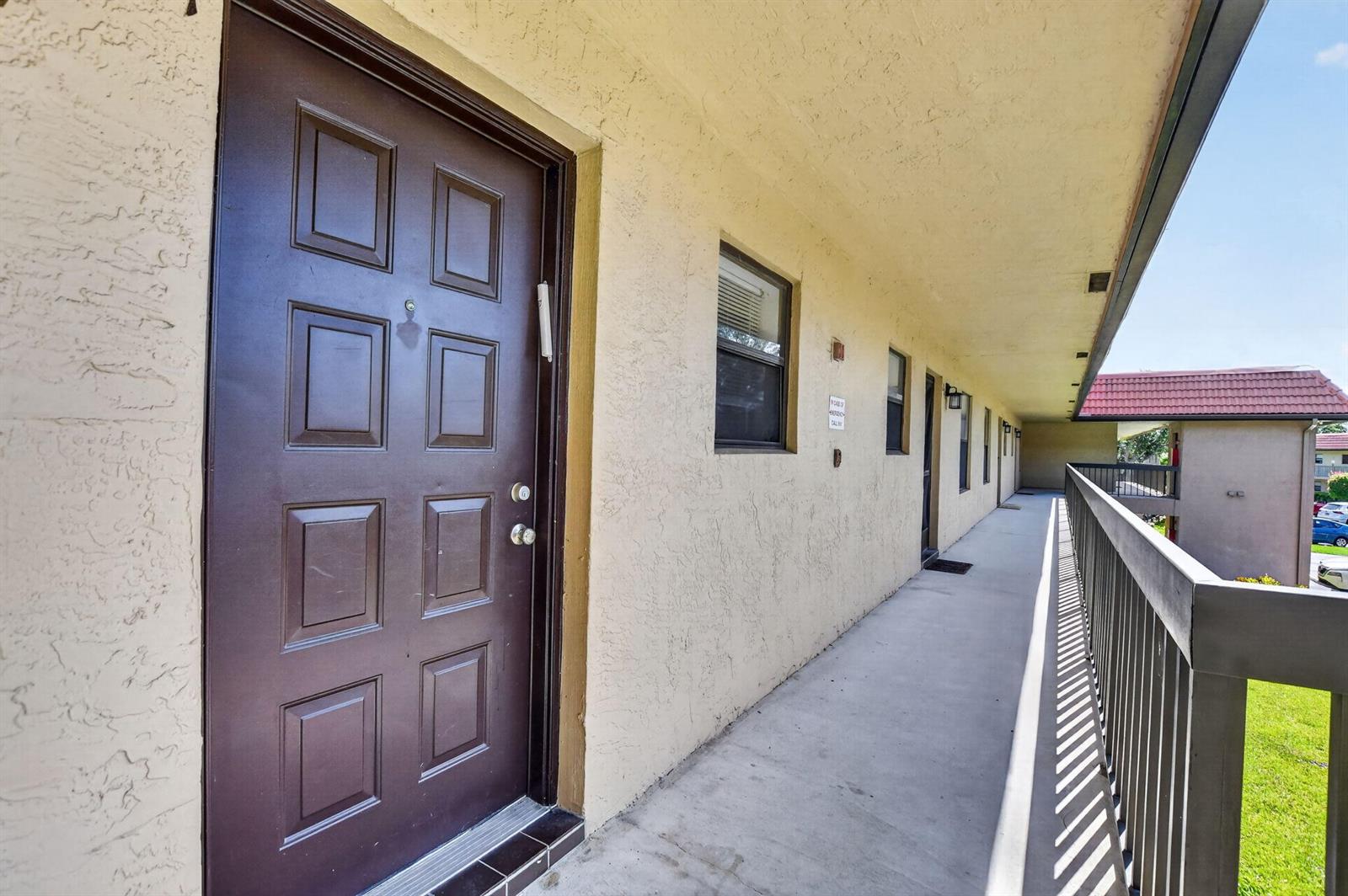 An exterior view of an apartment building walkway with a brown door and railing — 21895 Lake Forest Circle # 201, Boca Raton FL 33433, BOCA RATON, FL