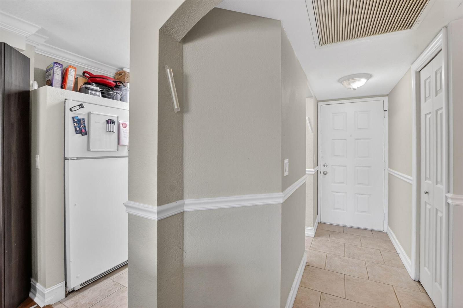 A view of a hallway with beige walls, tile flooring, a refrigerator, and a door — 21895 Lake Forest Circle # 201, Boca Raton FL 33433, BOCA RATON, FL