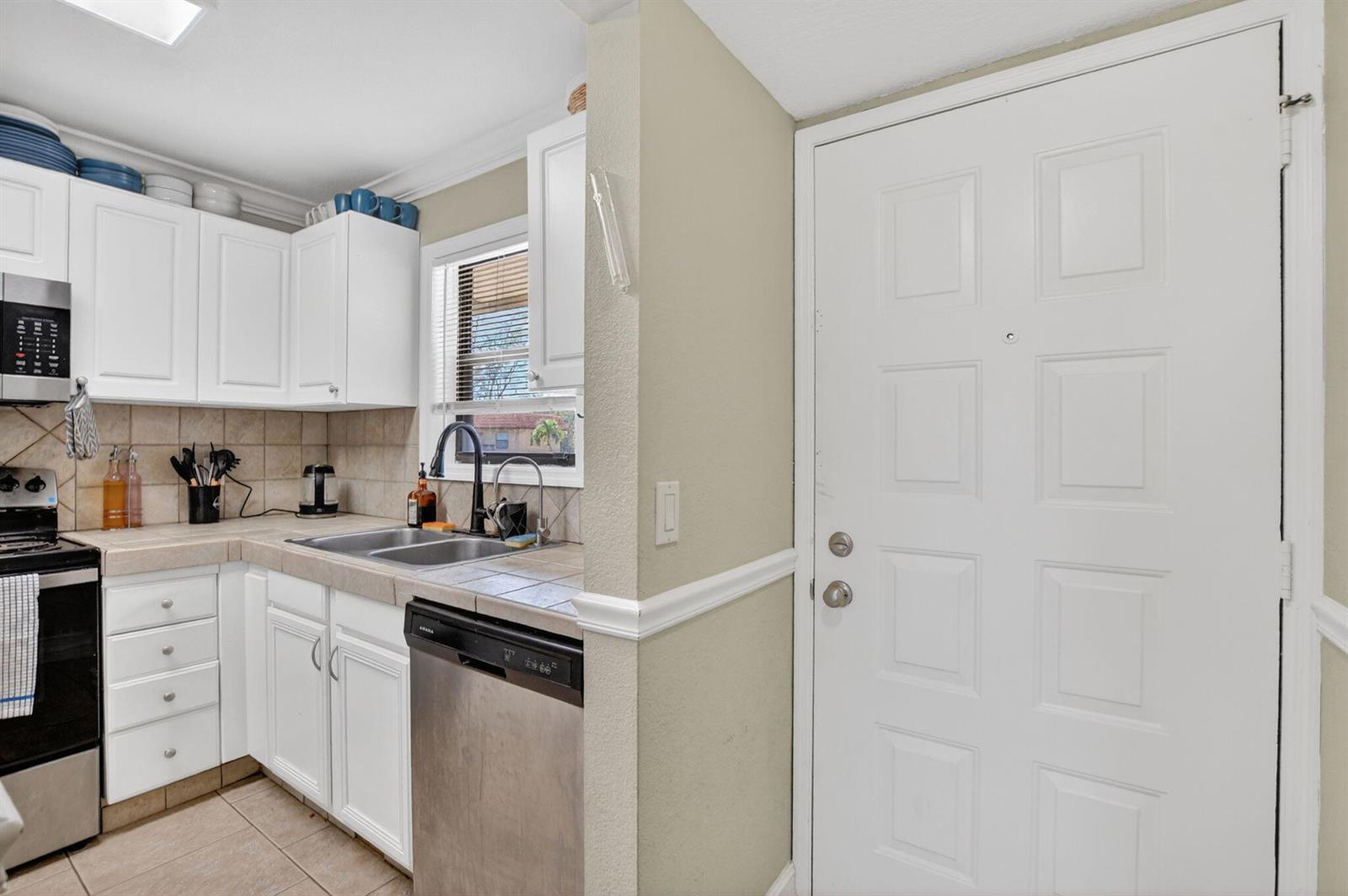 A kitchen features white cabinets, stainless steel appliances, tile countertops, and a white entry door — 21895 Lake Forest Circle # 201, Boca Raton FL 33433, BOCA RATON, FL