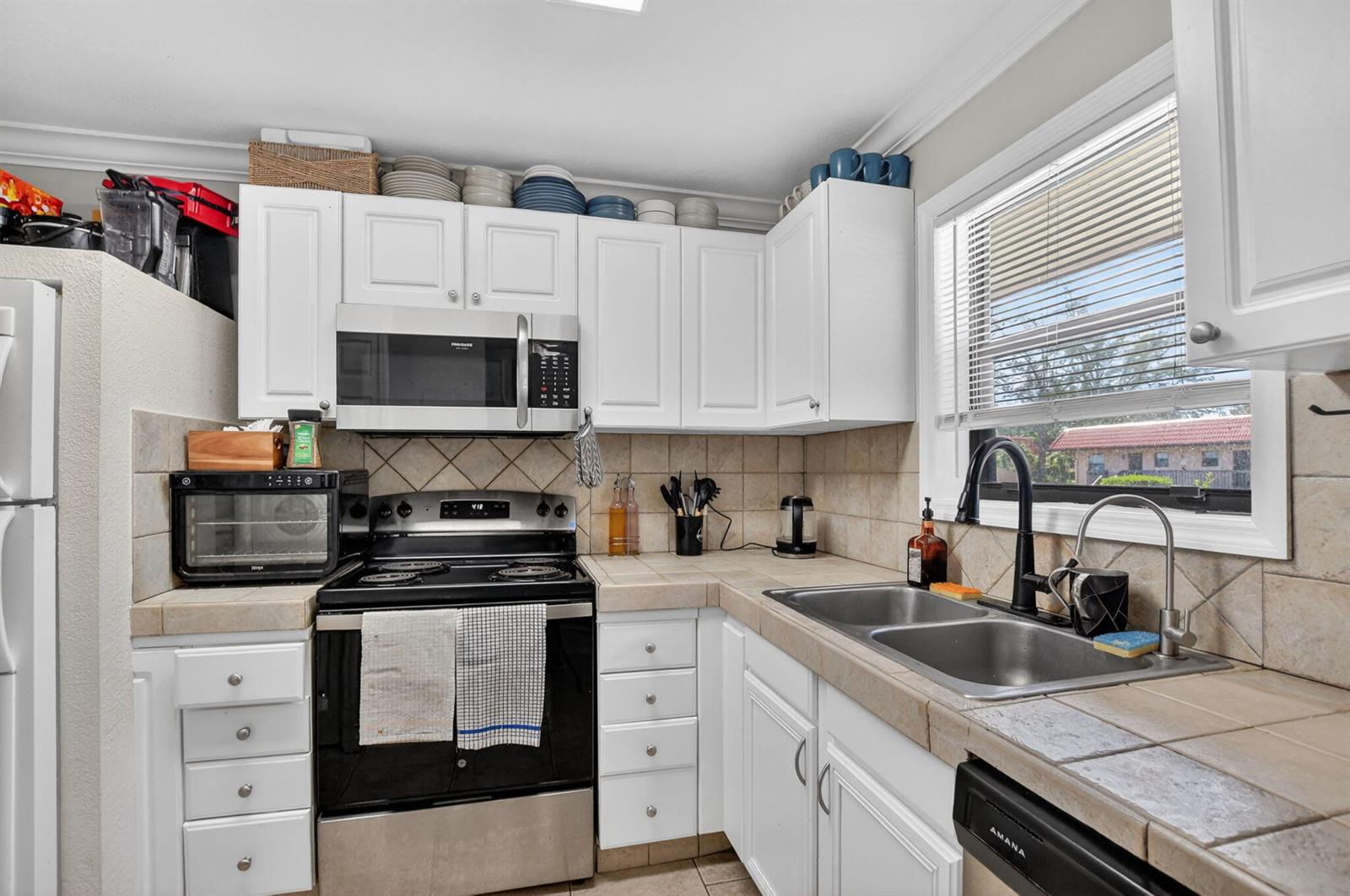 A kitchen features white cabinets, tile countertops, stainless steel appliances, and a double-basin sink — 21895 Lake Forest Circle # 201, Boca Raton FL 33433, BOCA RATON, FL