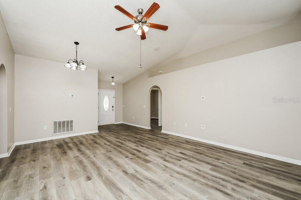 An empty living room features light-colored walls, wood-look flooring, and a ceiling fan — 12938 BRIDLEFORD DRIVE, GIBSONTON, FL