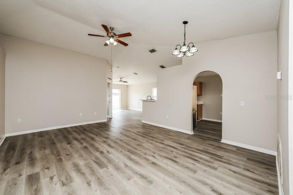 An open-concept living area features light gray wood-look flooring, vaulted ceilings, and a dining chandelier — 12938 BRIDLEFORD DRIVE, GIBSONTON, FL