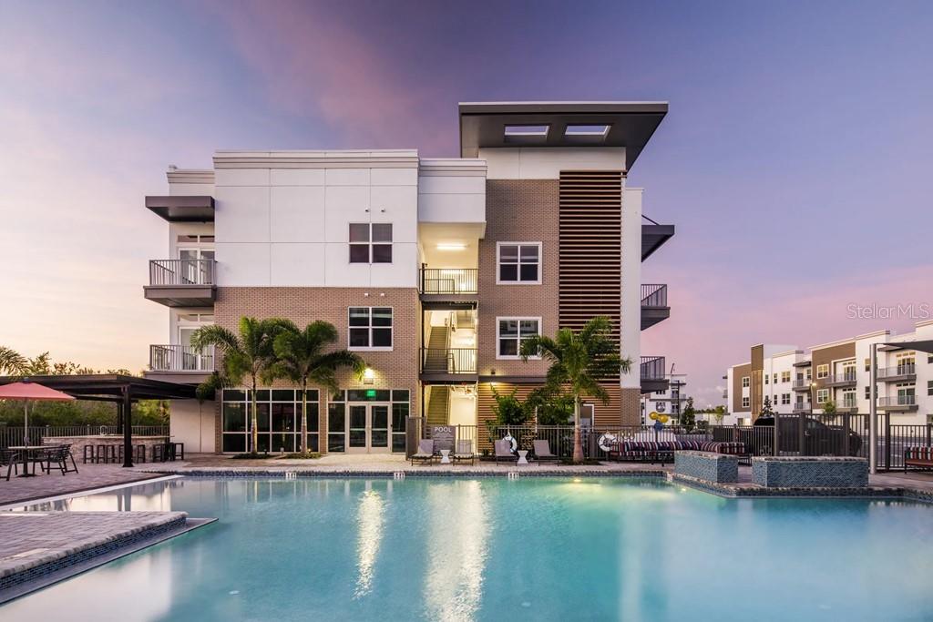 A modern apartment building exterior features a swimming pool, palm trees, and outdoor seating areas — 1185 S PINELLAS AVENUE UNIT B3, TARPON SPRINGS, FL