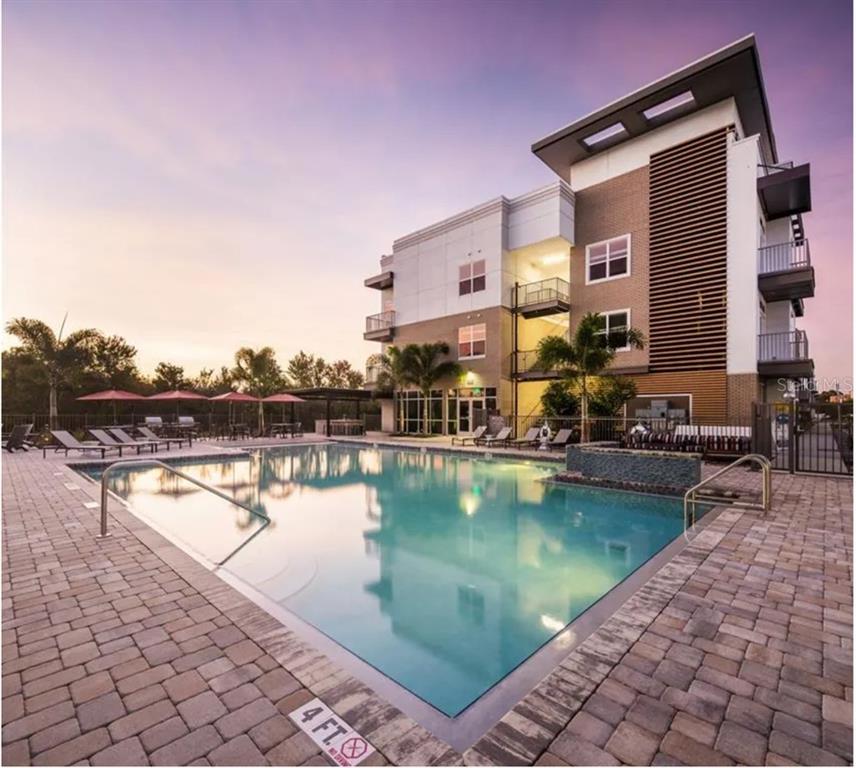 A multi-story apartment building overlooks a rectangular swimming pool with a paved deck at sunset — 1185 S PINELLAS AVENUE UNIT B3, TARPON SPRINGS, FL