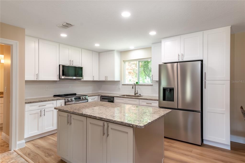 A kitchen with white cabinets, granite countertops, a central island, and stainless steel appliances — 10886 SW 90TH TERRACE, OCALA, FL