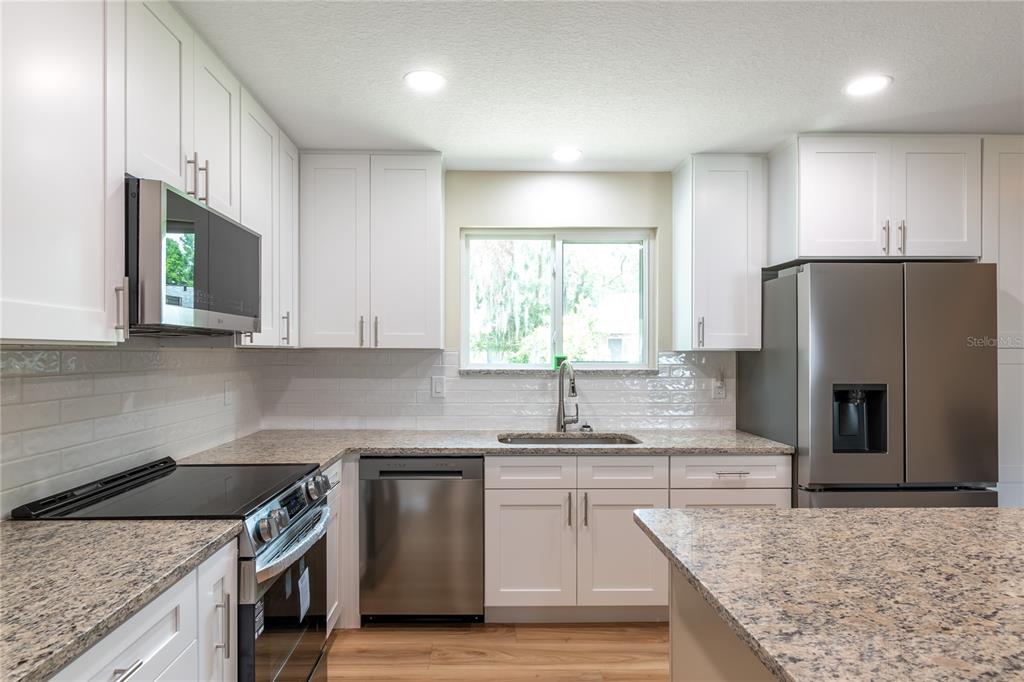 A kitchen features white cabinets, granite countertops, stainless steel appliances, and a subway tile backsplash — 10886 SW 90TH TERRACE, OCALA, FL