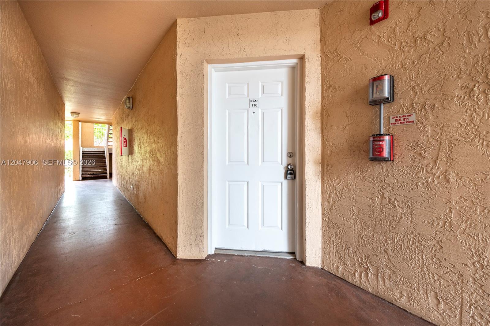 A white apartment door with a lockbox is located in an outdoor stucco hallway — 3480 N Pinewalk Dr N # 116, Margate FL 33063, MARGATE, FL