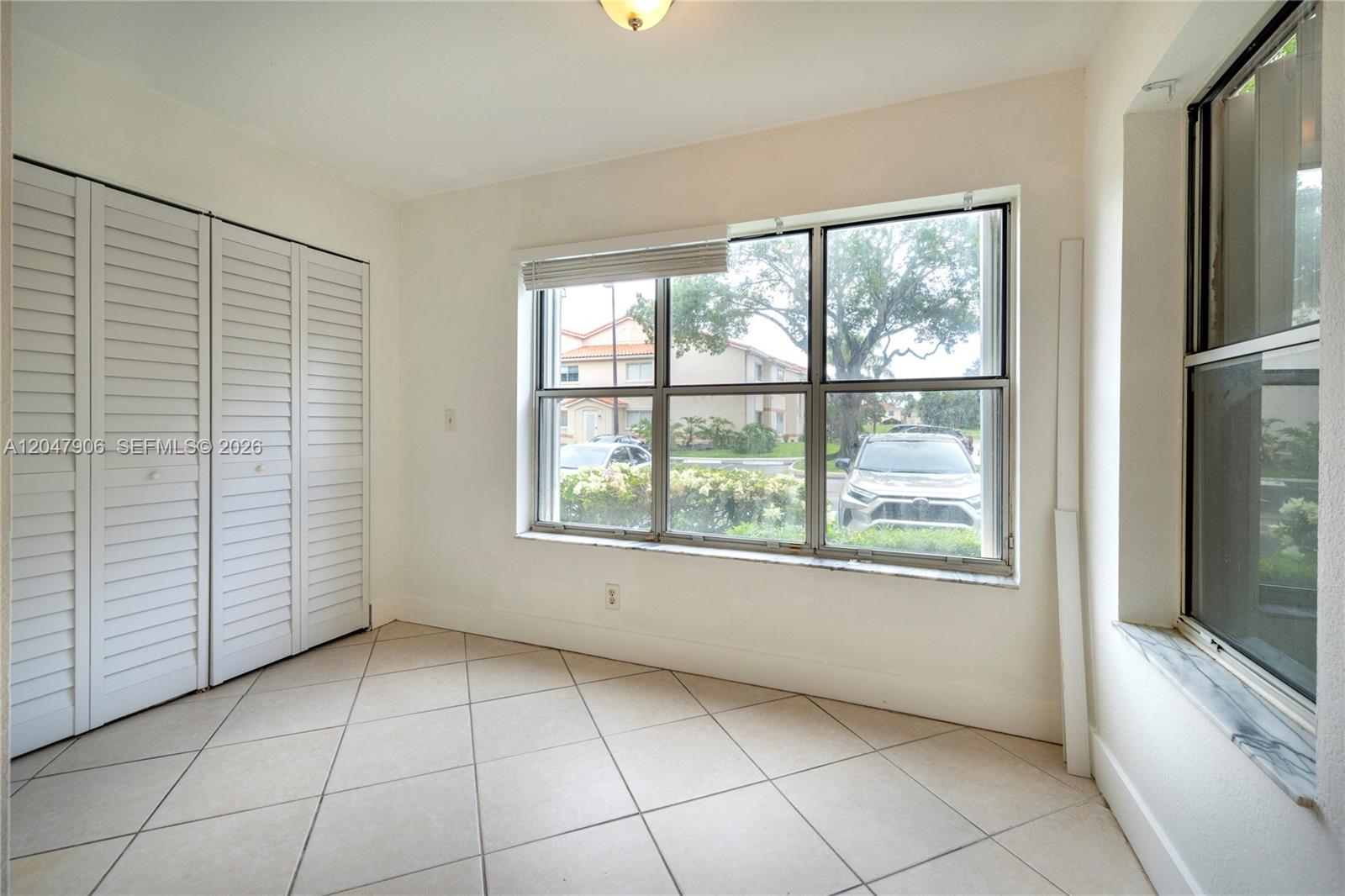 A room with white louvered closet doors, tile flooring, and large windows overlooking a parking area — 3480 N Pinewalk Dr N # 116, Margate FL 33063, MARGATE, FL