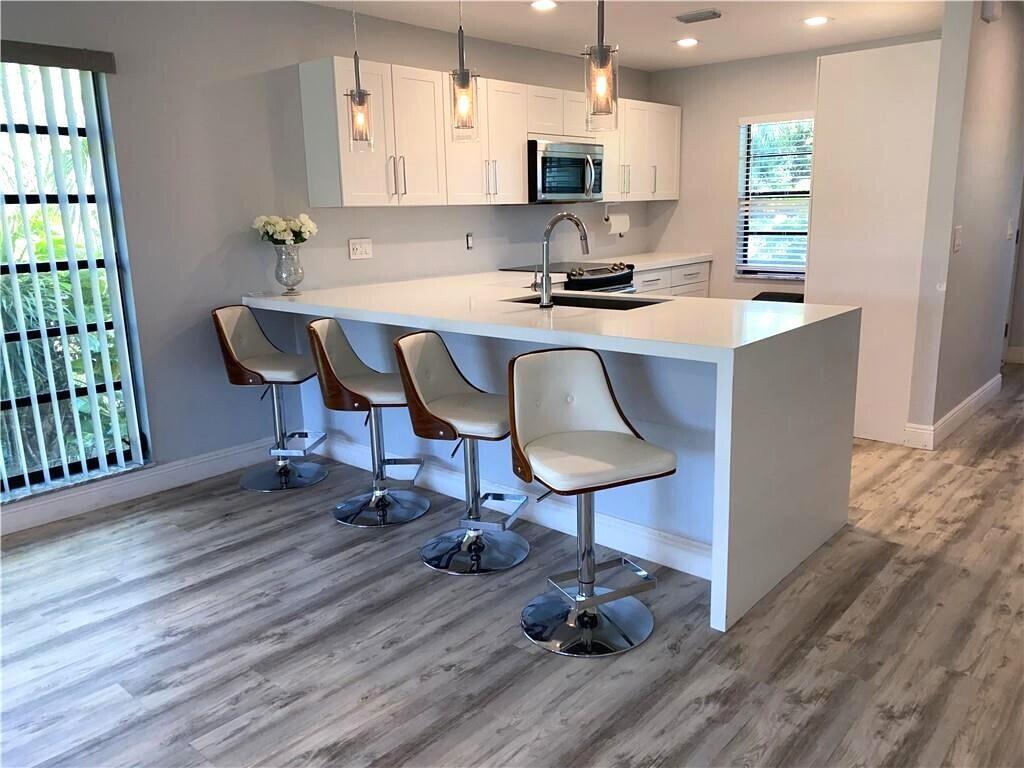 A modern kitchen features white cabinets, a waterfall island with bar stools, and wood-look flooring — 21766 Cypress Drive # g, Boca Raton FL 33433, BOCA RATON, FL