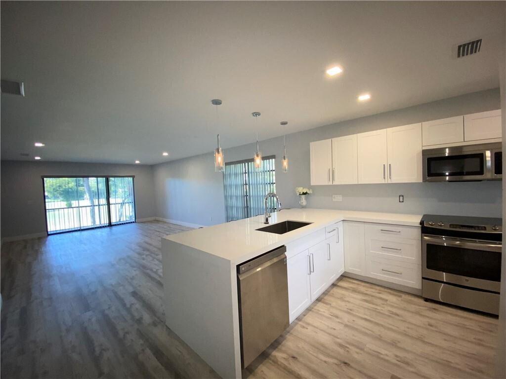 A modern kitchen with white cabinets and a quartz island overlooks an open living area — 21766 Cypress Drive # g, Boca Raton FL 33433, BOCA RATON, FL