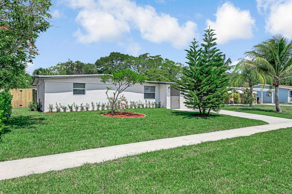 A single-story white house with a gray door, a front lawn, and a tall pine tree — 12063 Acapulco Avenue, Palm Beach Gardens FL 33410, PALM BEACH GARDENS, FL
