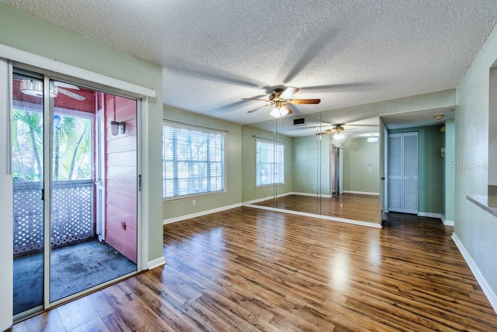 A room with wood-look flooring, a mirrored wall, a ceiling fan, and a sliding glass door — 3002 W CLEVELAND STREET UNIT C3, TAMPA, FL