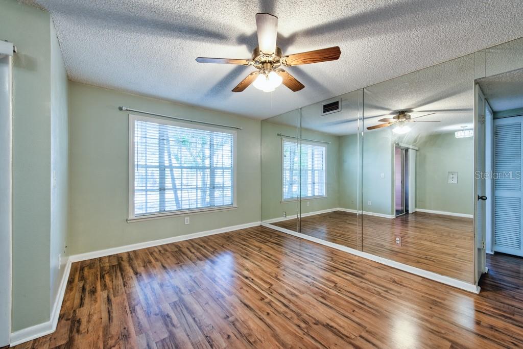 A room with light gray walls, wood-look flooring, a ceiling fan, and a mirrored wall — 3002 W CLEVELAND STREET UNIT C3, TAMPA, FL