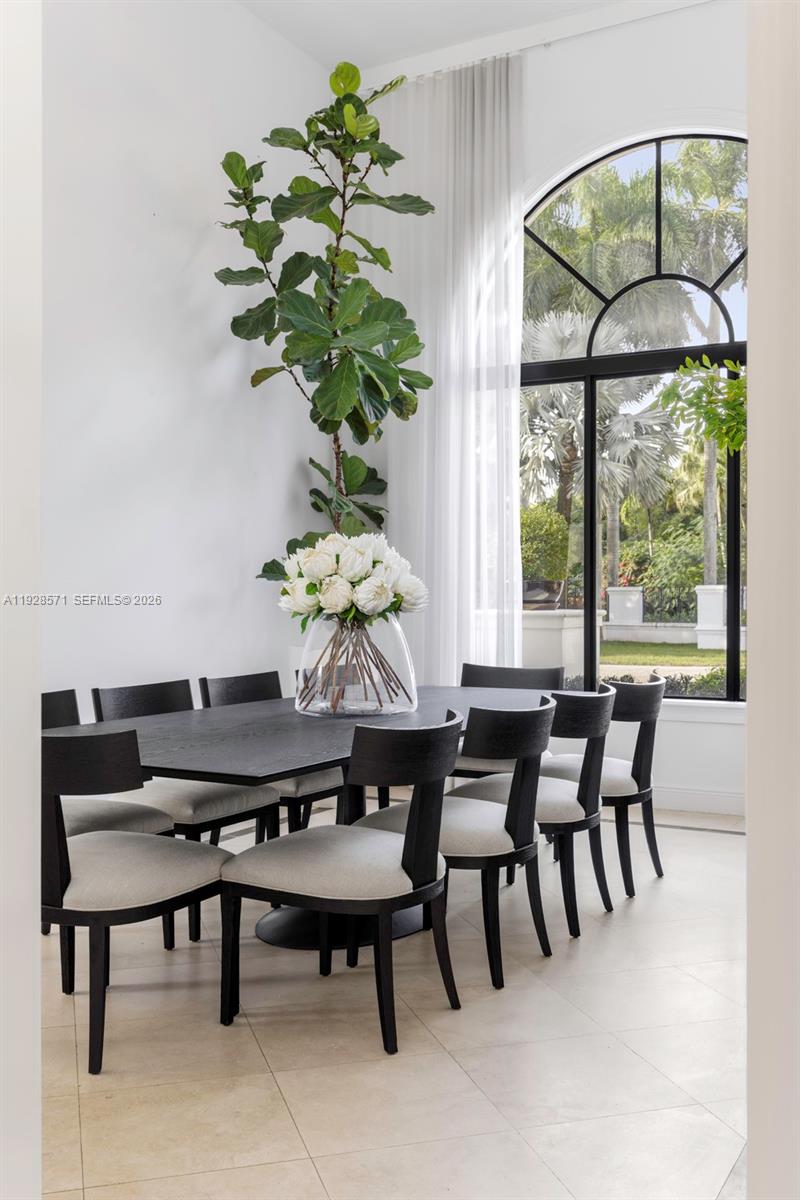 A dining room features a long black table, upholstered chairs, and a large arched window — 7430 SW 66th St, Miami FL 33143, MIAMI, FL